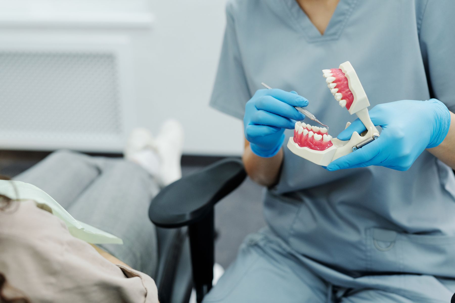 Dentist in blue gloves demonstrating brushing on a model of teeth