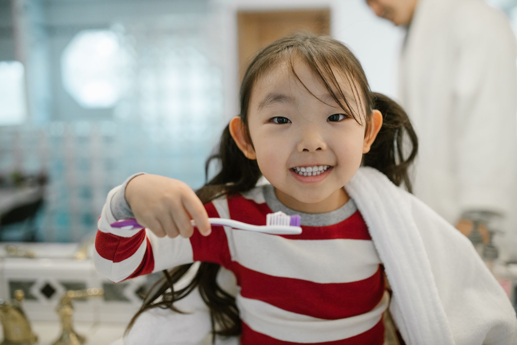 Smiling young girl holding a toothbrush in a bathroom