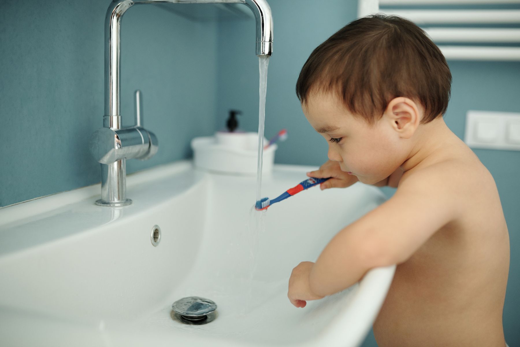 Toddler rinsing a toothbrush under a bathroom faucet
